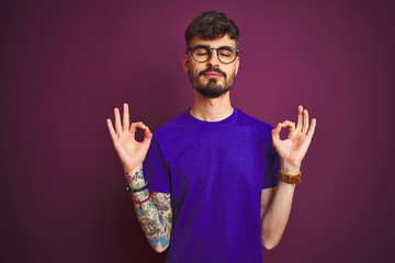 Young man with tattoo wearing t-shirt and glasses standing over isolated purple background relax...