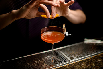 Fototapeta na wymiar Professional bartender spraying on the cocktail decorated with paper airplane in the clothespin with a orange zest juice