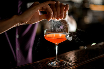 Professional male bartender spraying on the cocktail decorated with paper airplane in the clothespin with a orange zest juice