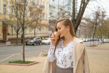 Young woman walking in the autumn city street and drinking take away coffee in paper cup.