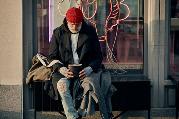 Mature caucasian vagrant man ask for some money donations from citizens, hopefully look at rusty empty jar. modern cafe behind him. Poverty, hungry, hope