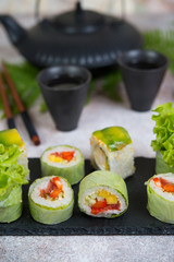 Vegetable vegetarian sushi rolls with a teapot of tea and Chinese cups stand on a concrete table.