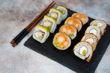 Vegetable vegetarian sushi rolls with a teapot of tea and Chinese cups stand on a concrete table.