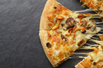 Mushroom pizza with melting cheese on the `black slate background