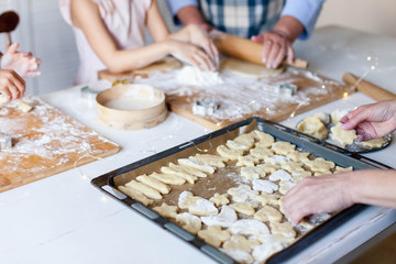 Family is cooking Christmas gingerbread cookies in home kitchen. Baking homemade biscuits on oven tray. Children chef concept. Close up of hands.