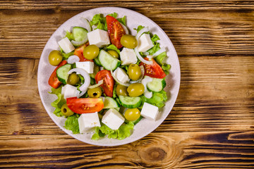 Ceramic plate with greek salad on wooden table. Top view