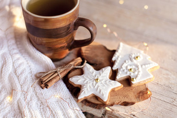Christmas still life. Gingerbread glazed cookies, cup of tea, cinnamon at wooden background with glares. Cozy tea time with homemade sweets and mug of hot beverage. Winter food, drink, new year lights