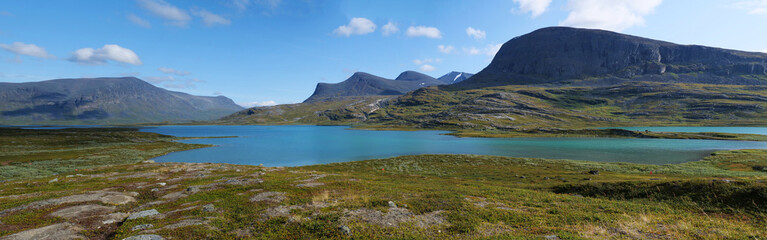 Lapland nature landscape wide panorama of blue glacial lake Allesjok near Alesjaure, birch tree forest, snow capped mountains. Northern Sweden, at Kungsleden hiking trail. Summer sunny day