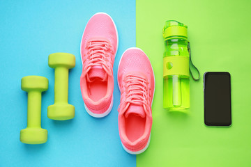 Sports water bottle, shoes, mobile phone and dumbbells on color background