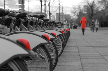 on a gloomy autumn day, a girl in a red coat takes a walk along a long row of bicycles with red lights standing in the Parking lot.