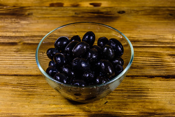 Glass bowl with black olives on wooden table