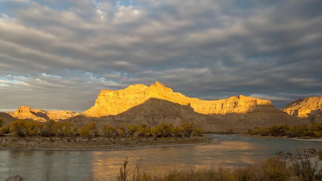 Timelapse as the sun lights up desert cliffs over the Green River as dark clouds roll through the sky in the Utah desert.