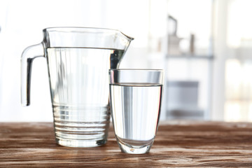Glass and jug of fresh water on table in room