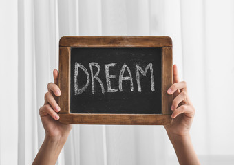 Female hands with word DREAM written on chalkboard