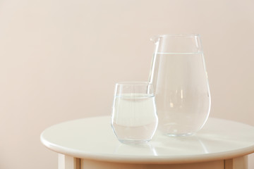 Glass and jug of fresh water on table against light background
