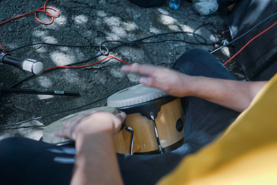 Sitting playing congas outside. Drum between the legs. African drums. Percussion instrument being played concept. Represented by percussionists hands hitting a drum.