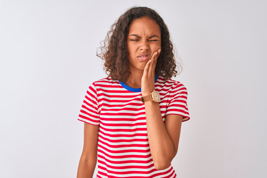 Young brazilian woman wearing red striped t-shirt standing over isolated white background touching mouth with hand with painful expression because of toothache or dental illness on teeth