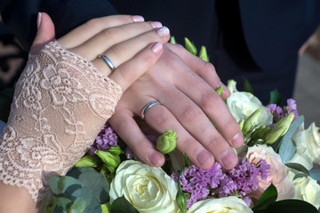 Obraz na płótnie Canvas Hands of the groom and the bride with wedding rings and a wedding bouquet from roses. Two wedding rings and spring blossoms. Wedding concept.