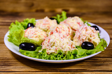 White plate with crab-cheese balls and lettuce leaves on wooden table