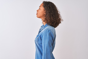 Young brazilian woman wearing denim shirt standing over isolated white background looking to side, relax profile pose with natural face and confident smile.