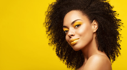 Summer portrait of African American Fashion Model  . Brunette young woman with afro hair style,creative yellow make up, lips and eyeshadows on colorful background. Summer beauty concept