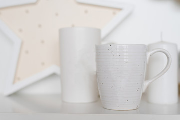 Two white mugs stand on a white shelf in the living room or dining room
