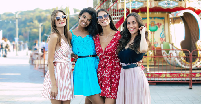 This is us. Four stunning women with long hair and in dresses of vivid colors are posing for a joint photo at the funfair.