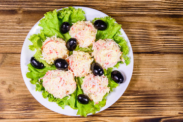 White plate with crab-cheese balls, black olives and lettuce leaves on wooden table. Top view