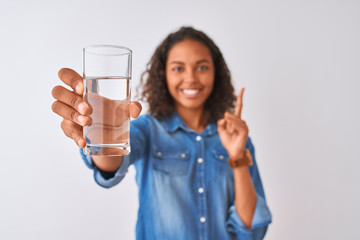 Young brazilian woman holding glass of water standing over isolated white background surprised with an idea or question pointing finger with happy face, number one