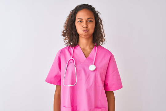 Young brazilian nurse woman wearing stethoscope standing over isolated white background puffing cheeks with funny face. Mouth inflated with air, crazy expression.