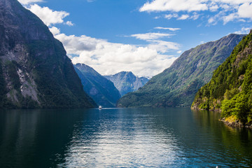 Scenic landscape View on the mountain peaks with green slopes and surface of water and feather clouds on the sky on background in sunny day. Neroyfjord - the narrowest fjord in Norway, Gudvangen Flam