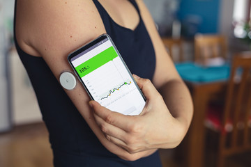 Woman checking glucose level with a modern technology remote sensor and mobile phone, without blood. Diabetes treatment. - obrazy, fototapety, plakaty