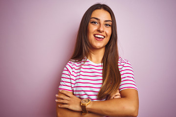 Obraz premium Young beautiful woman wearing striped t-shirt standing over isolated pink background happy face smiling with crossed arms looking at the camera. Positive person.