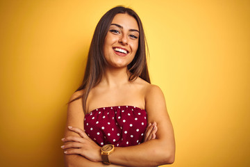 Young beautiful woman wearing red t-shirt standing over isolated yellow background happy face smiling with crossed arms looking at the camera. Positive person.