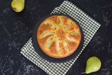 Homemade pear pie on a black table with pears in the background.