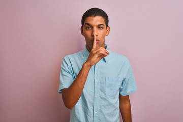 Young handsome arab man wearing blue shirt standing over isolated pink background asking to be quiet with finger on lips. Silence and secret concept.