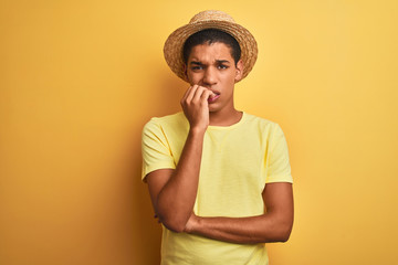 Young handsome arab man wearing t-shirt and summer hat over isolated yelllow background looking stressed and nervous with hands on mouth biting nails. Anxiety problem.