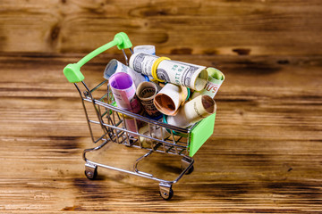 Many rolled up banknotes in small shopping cart. Euro, american dollars, ukrainian hryvnias, egyptian pounds, russian roubles