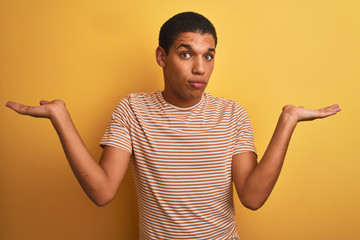 Young handsome arab man wearing striped t-shirt standing over isolated yellow background clueless...