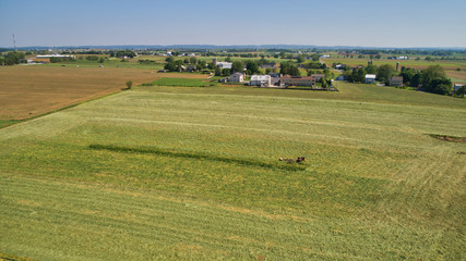 Obraz premium Aerial View of an Amish Farm Harvesting his Crop using Horses and Antique Equipment as Seen by a Drone