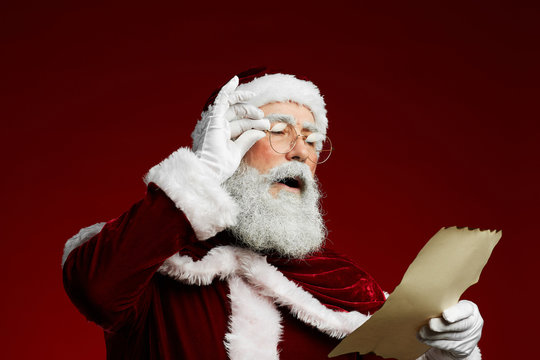 Waist up portrait of classic Santa reading list on parchment standing against red background, copy space