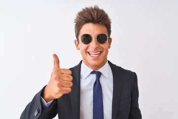 Young handsome businessman wearing suit and sunglasses over isolated white background doing happy thumbs up gesture with hand. Approving expression looking at the camera with showing success.