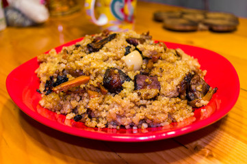 Uzbek pilaf with meat in a red plate on a wooden table, close up