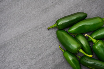 A pile of spicy green jalapenos on a gray slate background with copy space