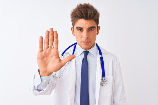 Young handsome doctor man wearing stethoscope over isolated white background doing stop sing with palm of the hand. Warning expression with negative and serious gesture on the face.