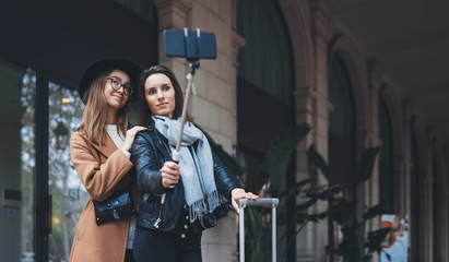 Fototapeta na wymiar Girlfriends tourist taking photo selfie together on smartphone mobile. Blogger hipster travels in europe city hotel. Vacation holiday friendship concept. Travelers self cellphone internet mockup space