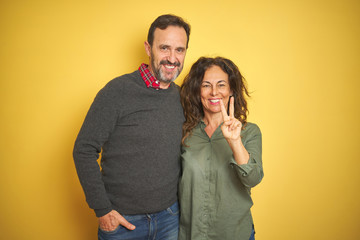 Beautiful middle age couple over isolated yellow background showing and pointing up with fingers number two while smiling confident and happy.