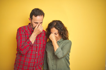 Beautiful middle age couple over isolated yellow background tired rubbing nose and eyes feeling fatigue and headache. Stress and frustration concept.