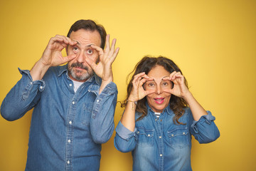Beautiful middle age couple together standing over isolated yellow background Trying to open eyes with fingers, sleepy and tired for morning fatigue
