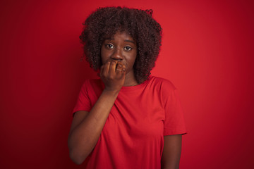 Fototapeta na wymiar Young african afro woman wearing t-shirt standing over isolated red background looking stressed and nervous with hands on mouth biting nails. Anxiety problem.